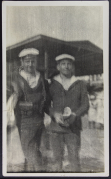 Blurry photograph depicting two French seafarers with their traditional uniform and beret on shore 