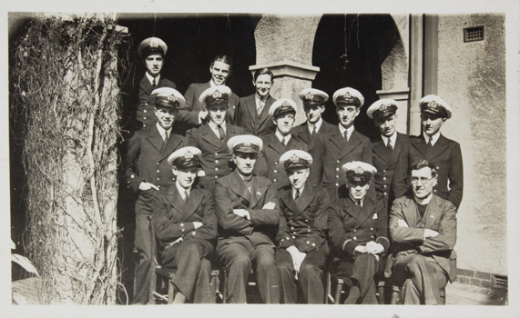 Group of officers in uniform sitting and standing in the cloister of the Flinders Street Mission with one of the reverend.