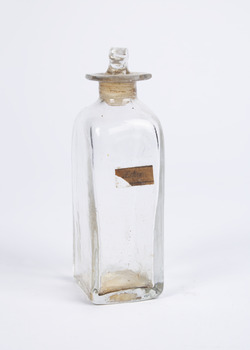 Clear glass  squares-base medicine container  with glass lid. A paper label on one side says "ether".