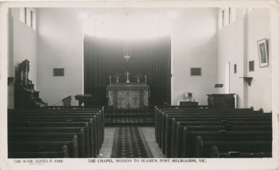 Black and white postcard depicting the inside of the chapel in the 1937 Port Melbourne Mission with pews, reed organ and altar.
