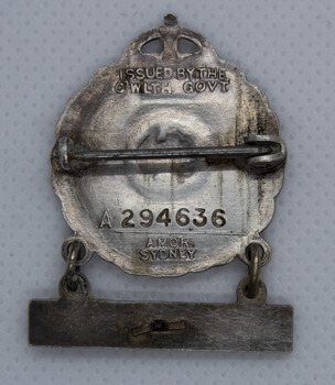 Back of small silver badge with hanging bar, showing maker and issue number