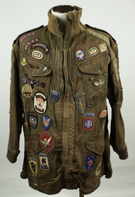 Long sleeve, mid-length, front-zip fastening khaki jacket, adorned with many cloth and metal badges relating to parachuting.