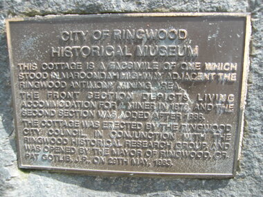 Photograph, The official plaque of the facsimile of the miner's hut, located at the back of Ringwood Lake, from the original that once stood on Maroondah Highway in the 1870s onwards. The cottage was erected by the Ringwood City Council in conjunction with Ringwood Historical Research Group (now Ringwood & District Historical Society). Officially opened by Mayor Cr Pat Gotlib JP on 29th May 1983