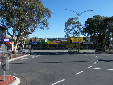 Photograph, Corner of Railway Place and Maroondah Highway, Ringwood at the former entrance to the railway station, showing shops on the other side of the road (now REALM library)