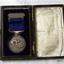 Medal is mounted ion blue velvet opposite a cream satin lined lid
