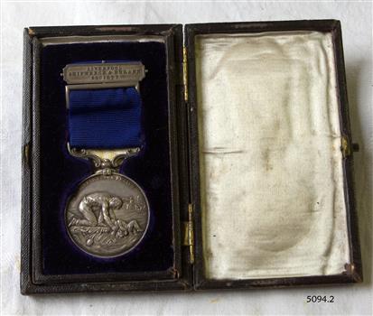Medal is mounted ion blue velvet opposite a cream satin lined lid