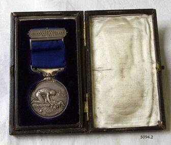 Medal is mounted ion blue velvet opposite a cream satin lined lid