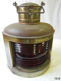 Brass lamp with red louvered glass on the front, flip lid and carry handle