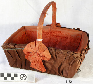 Rectangular basket, orange-brown fabric lining  covered outside with brown fabric, rosettes at base of handle
