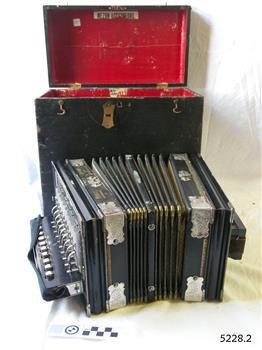 Open, red-lined black case, black and cream accordion in front, opened out