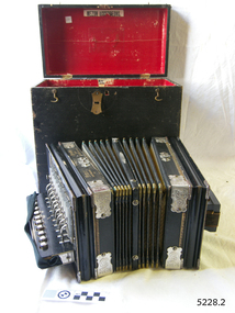 Open, red-lined black case, black and cream accordion in front, opened out