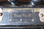 Gold embossed stamp on black fabric, perhaps leather, is attached to the accordion by metal studs