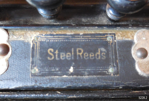 Gold embossed stamp on black fabric, perhaps leather, is attached to the accordion by metal studs