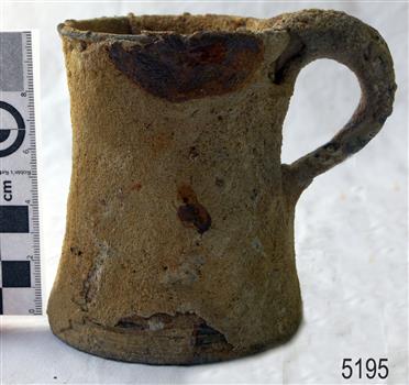 Metal tankard is heavily encrusted. The edge of the base is chipped.