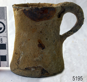 Metal tankard is heavily encrusted. The edge of the base is chipped.