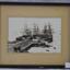 Black and white photograph, framed, behind glass. showing tall ships berthed at a pier