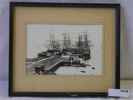 Black and white photograph, framed, behind glass. showing tall ships berthed at a pier