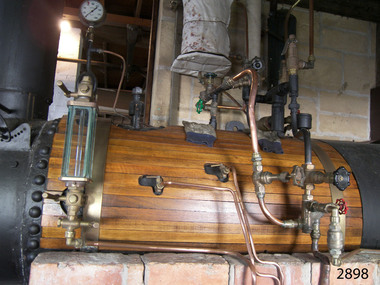 Cylindrical horizontal boiler with varnished timber encasing and shiny copper pipes