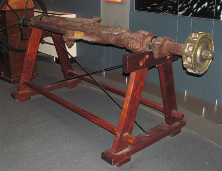 The long steering gear is supported by a wooden stand with metal brading