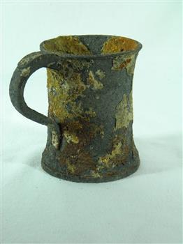 Metal tankard with rolled lip and flared base. Has encrustations.