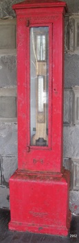 Red, cast metal case with hinged glass front door, displaying barometer's values