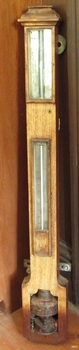 Barometer is in wooden casing, with two glass panels revealing instruments within