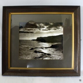 Sepia photograph of sea, shore and cliffs, framed behind glass