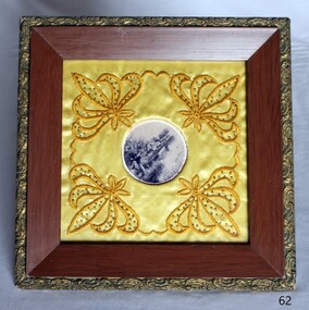 picture mounted on embroidered, padded fabric and framed in wood with a decorative border