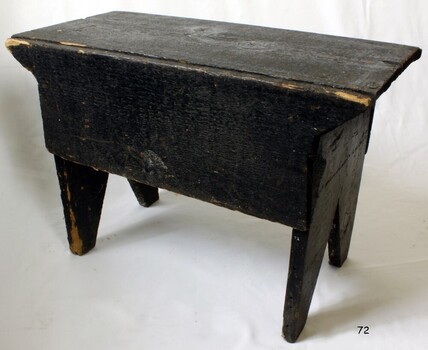 Bench painted black, seat is rectangular, legs taper inwards towards base