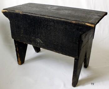 Bench painted black, seat is rectangular, legs taper inwards towards base