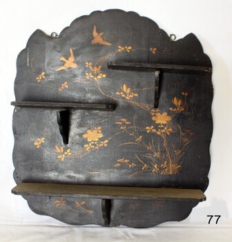 Black painted wooden shelves on irregular shaped panel. Gold decoration of doves and flowers is painted on the panel.