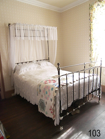 Black iron bed has white paint at the joins and a narrow canop at the top