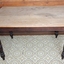 Oblong wooden table on four dark brown legs. The table surface appears to have been scrubbed clean multiple times, resulting in it being reduced to light coloured bare wood.