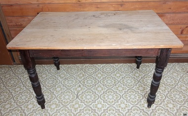 Oblong wooden table on four dark brown legs. The table surface appears to have been scrubbed clean multiple times, resulting in it being reduced to light coloured bare wood.