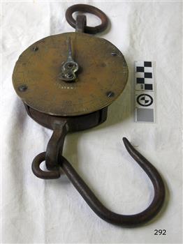 Round brass scale with a ring on top and a hook below, and inscriptions stamped and embossed on its face.