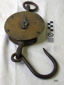 Round brass scale with a ring on top and a hook below, and inscriptions stamped and embossed on its face.