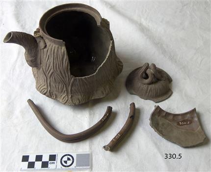 Brown clay teapot with vertical wave design. Pot is broken.