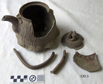 Brown clay teapot with vertical wave design. Pot is broken.