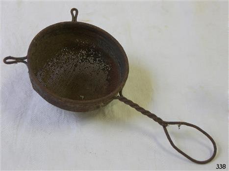 A small metal mesh strainer, with a twisted wire handle and two wire lips to allow it to be balanced over a cup or bowl.