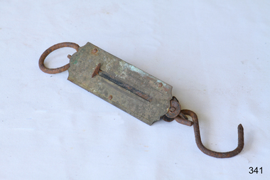 A corroded metal instrument with a spring and hook that shows the weight of any item placed on the hook.