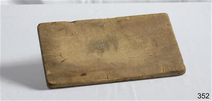 An oblong wooden bread board, well used and worn.