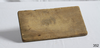 An oblong wooden bread board, well used and worn.