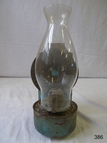 Lamp with blue metal tank and base for the rear reflector, and a narrow bulbous glass lamp cover