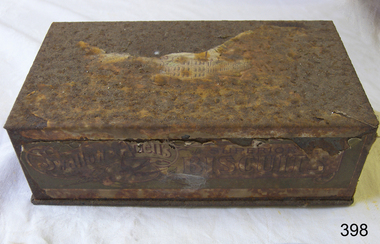 A rusted rectangular tin with an inscription on lid and front edge.