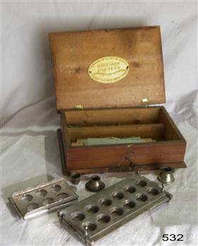 An oblong wooden box with hinged lid containing equipment for making capsules and cachets.