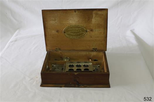 An oblong wooden box with hinged lid containing equipment for making capsules and cachets.