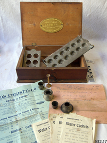 An oblong wooden box with hinged  lid containing equipment for making capsules and cachets. 