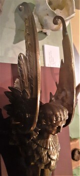 Wings have feather detail and curl around at tips, figure's face is looking downwards.