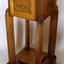 Timber pedestal with flat square base, legs in each corner, supporting square box with cut corners, decorative pattern on sides and lid on top.
