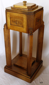 Timber pedestal with flat square base, legs in each corner, supporting square box with cut corners, decorative pattern on sides and lid on top.
